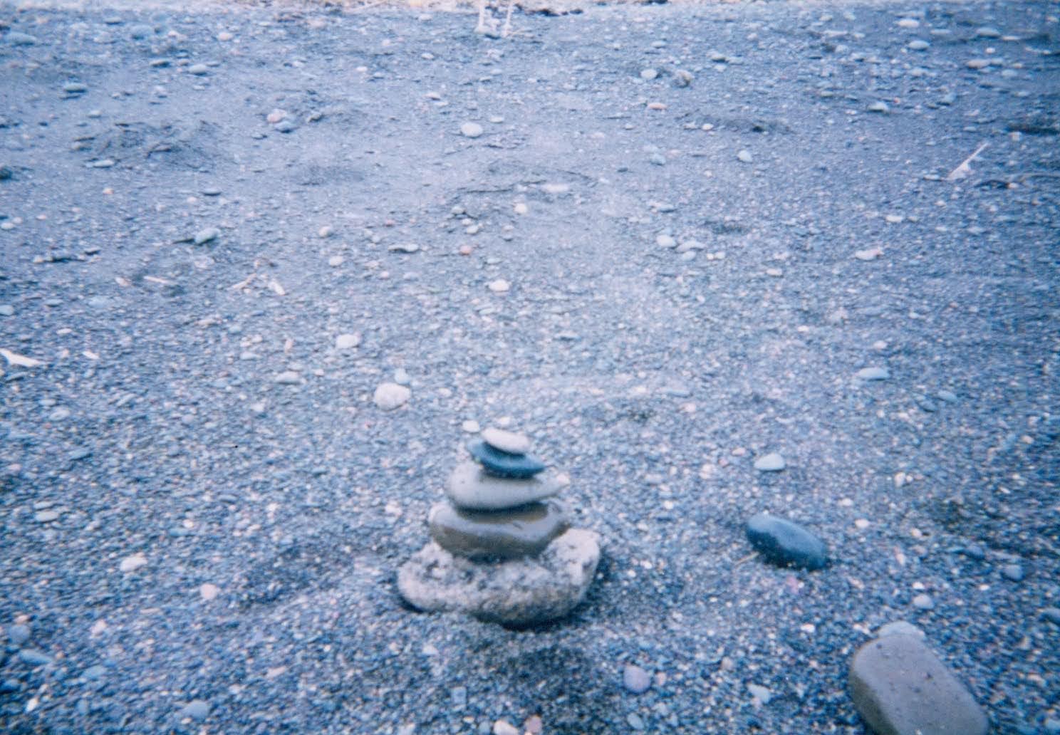 北海道の支笏湖畔、灰色の火山砂礫地に不自然に積み上げられた石の塔。周囲に遮蔽物のない無機質な風景の中で、方向感覚を維持するための目印として機能している様子。