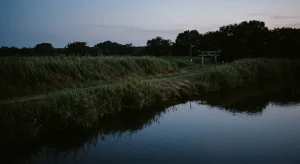 夕暮れ時の静寂に包まれた河畔の風景と遠くに見える古風な集落の遠景