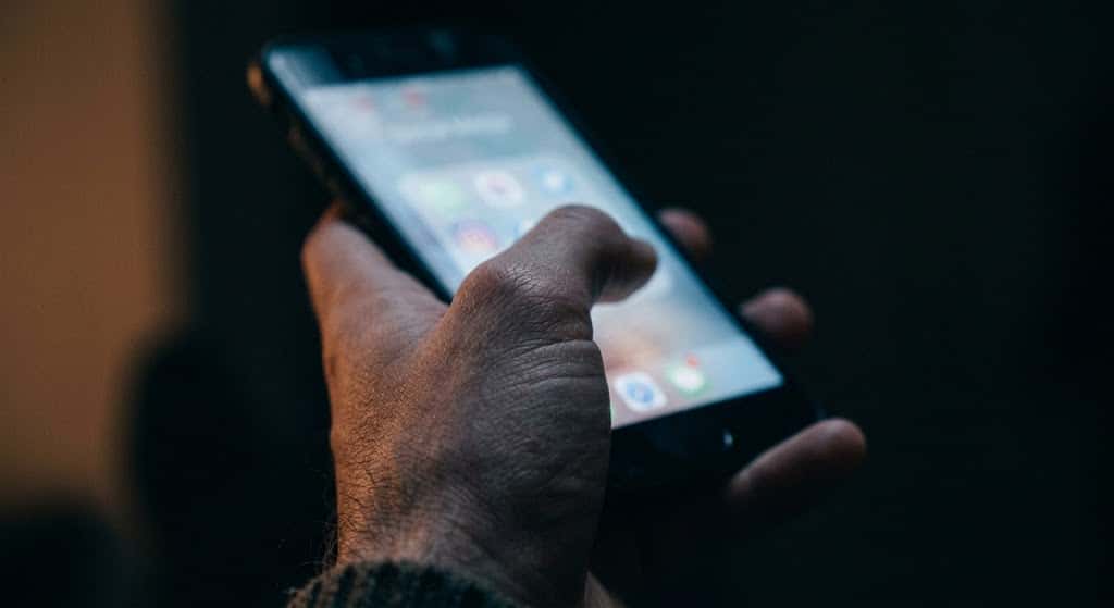 薄暗い室内でスマートフォンを手にする人物の手元と静まり返った空間