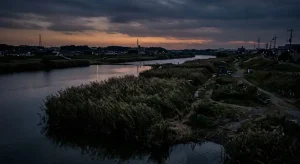 夕暮れ時の静けさに包まれた河川敷と薄暗い水面を描く河童伝承の背景イメージ