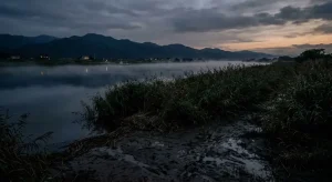 夕暮れの湿った河原と薄暗い川面が広がる哀愁と不穏の混ざる遠景